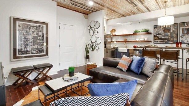 A modern living room with a sofa, coffee table, and a dining area with chairs and a table. - Contemporary 3BR Condo | Downtown Near Nightlife (Savannah)