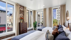 A hotel room with two beds, large windows, a brick wall, and a view of the city. - Contemporary 3BR Condo | Downtown Near Nightlife (Savannah)
