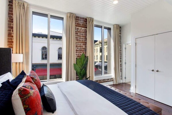 Habitación de hotel con una cama grande, un armario, una ventana con cortinas y vistas a edificios.