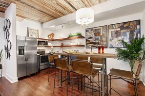A modern kitchen with a stainless steel refrigerator, a microwave, and a wooden ceiling. There are bar stools and a bar counter. - Contemporary 3BR Condo | Downtown Near Nightlife (Savannah)
