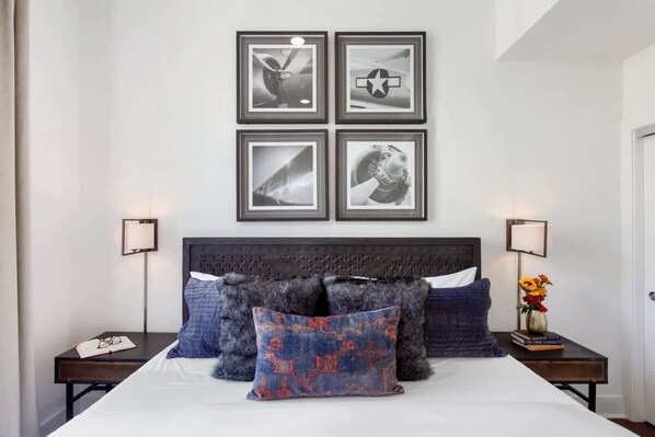 Une chambre à coucher bien rangée, avec un grand lit, une tête de lit sombre et quatre tableaux encadrés accrochés au mur.