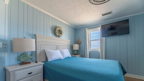 Une chambre à coucher avec un lit, des tables de chevet, une télévision et une fenêtre.