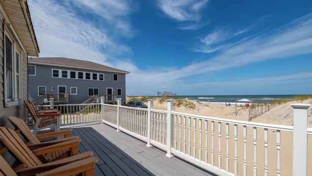 Une terrasse en bois avec des chaises, un bâtiment doté d’un balcon et une vue sur la plage.