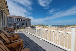 Eine Holzterrasse mit Stühlen, ein Gebäude mit Balkon und Blick auf den Strand.