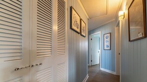 Un couloir avec des portes blanches, des œuvres d’art encadrées et un luminaire.