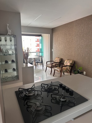 A modern kitchen with a gas stove, a glass display cabinet with kitchenware, and a dining area with chairs and a table. - 2-bedroom apartment - excellent location, just 2 km from Shopping da Bahia. (Salvador)