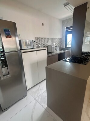 A modern kitchen with a refrigerator, microwave, toaster, and gas stove. - 2-bedroom apartment - excellent location, just 2 km from Shopping da Bahia. (Salvador)
