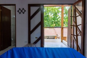 A room with a bed, a door, and a view of a garden through an open door. - Casa com 2 suítes e Churrasqueira no Figueira (Ubatuba)