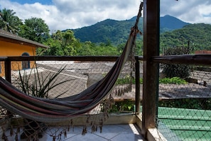 A hammock on a balcony with a view of mountains and greenery. - Casa com 2 suítes e Churrasqueira no Figueira (Ubatuba)