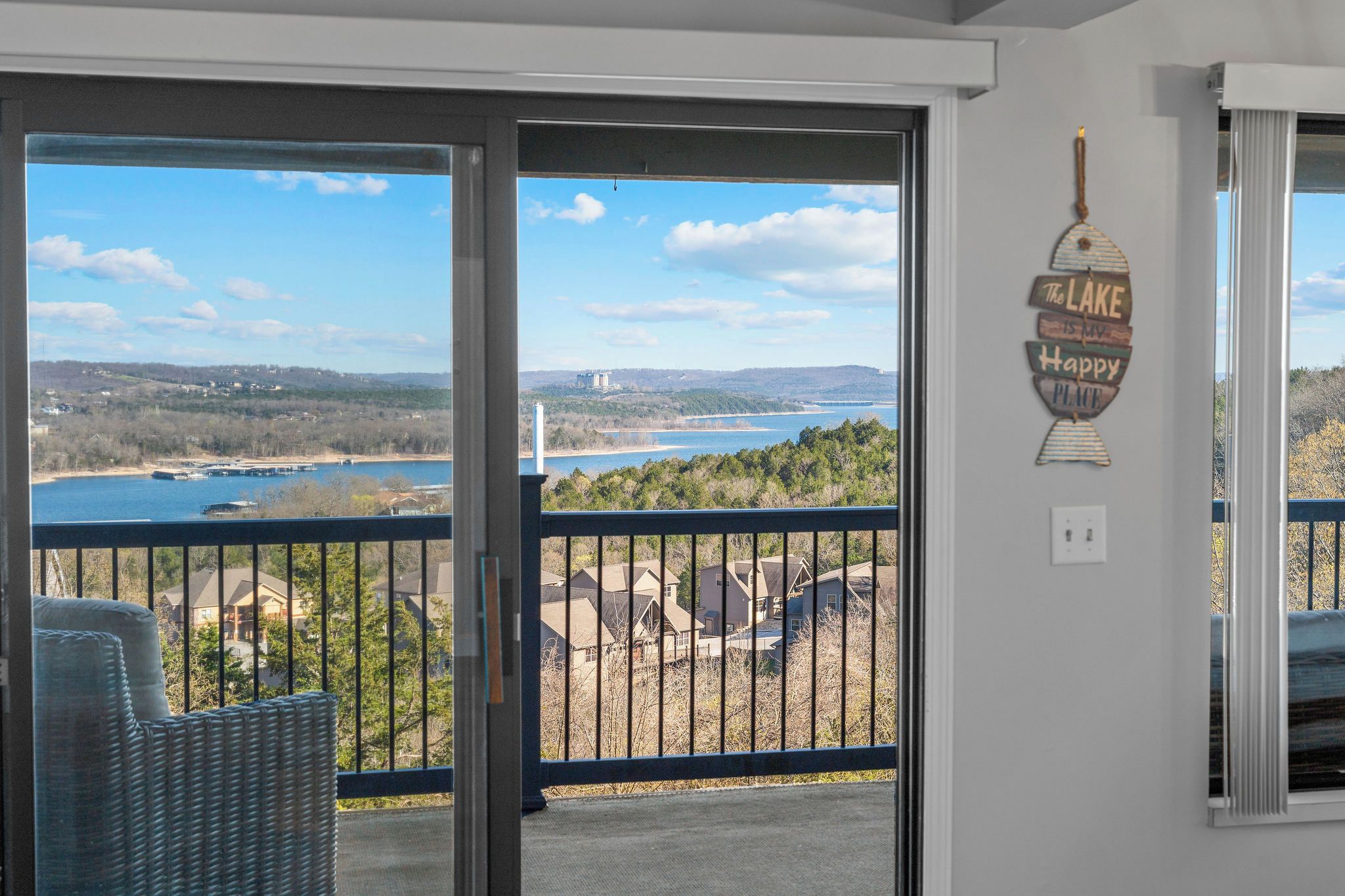 A room with a view of a lake and hills, a wicker chair, and a sign on the wall.
