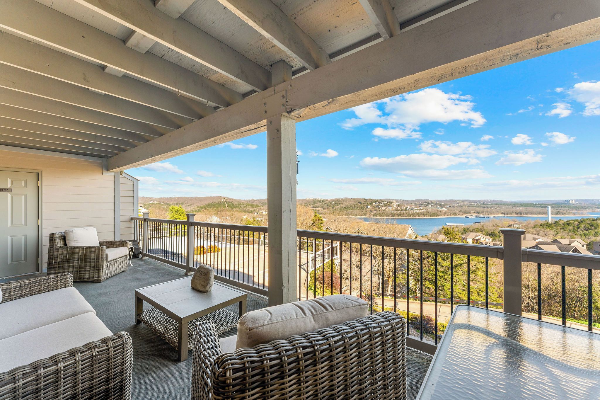 A covered outdoor seating area with wicker furniture and a view of a lake.