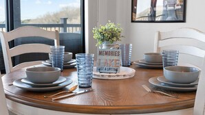 Una mesa de comedor preparada con fuentes, vasos y cubiertos, una planta en maceta y un cartel enmarcado.