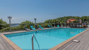 Piscina retangular com um deck de madeira, rodeada por espreguiçadeiras e um cercado.