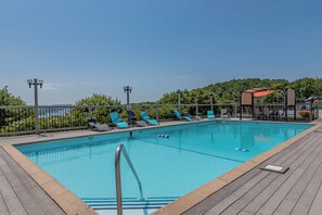 Piscina retangular com um deck de madeira, rodeada por espreguiçadeiras e um cercado.
