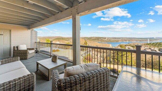 Un espacio al aire libre techado con muebles de mimbre, una mesa y vistas a un lago y un paisaje lejano.