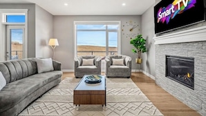 A living room with a sofa, two armchairs, a coffee table, a fireplace, a TV, and a large window with a view.