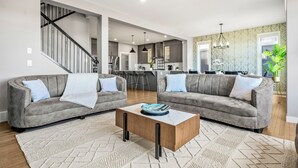 A modern living room with two grey sofas, a wooden coffee table, and a staircase leading to an upper floor.
