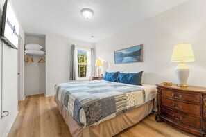 Ein Schlafzimmer mit Bett, Nachttisch, Kommode, Fenster und einem Bild an der Wand.