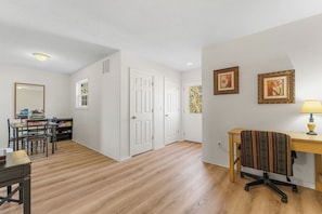 Ein Zimmer mit Holzboden, weißen Wänden, einem Schreibtisch mit Lampe, einem Stuhl und einem Bücherregal mit Gesellschaftsspielen.