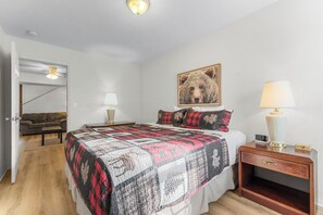 Un dormitorio con cama, una mesita de noche con lámpara, una puerta que da a otra habitación y un cuadro colgado en la pared.