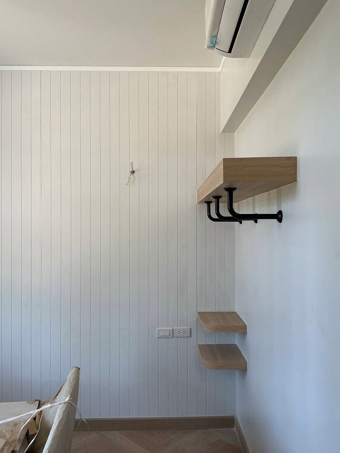A room with vertical paneling on the walls, a wooden shelf unit, and a black metal rack.