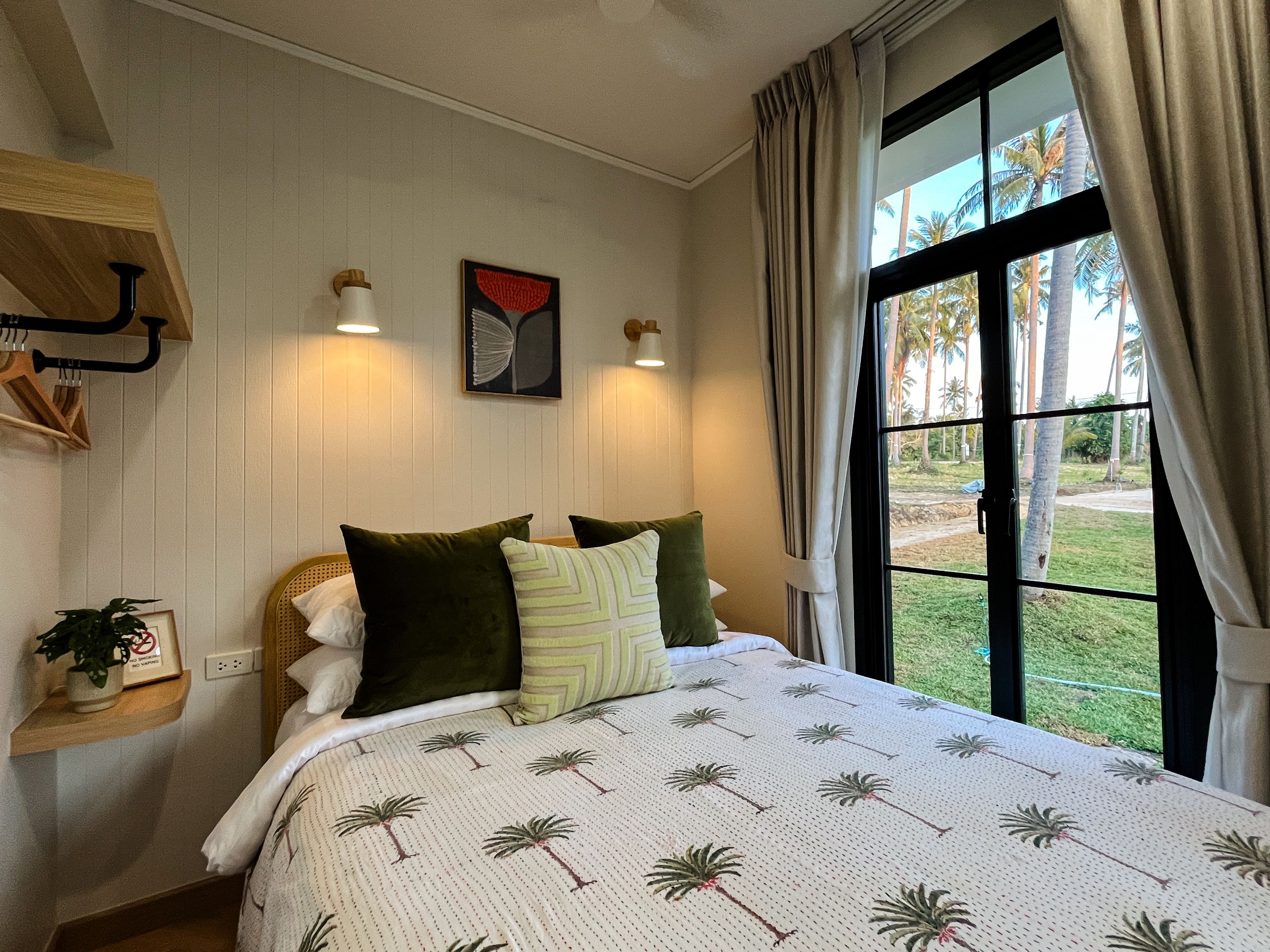 A bedroom with a bed, a window with curtains, a wall-mounted light fixture, and a framed picture.