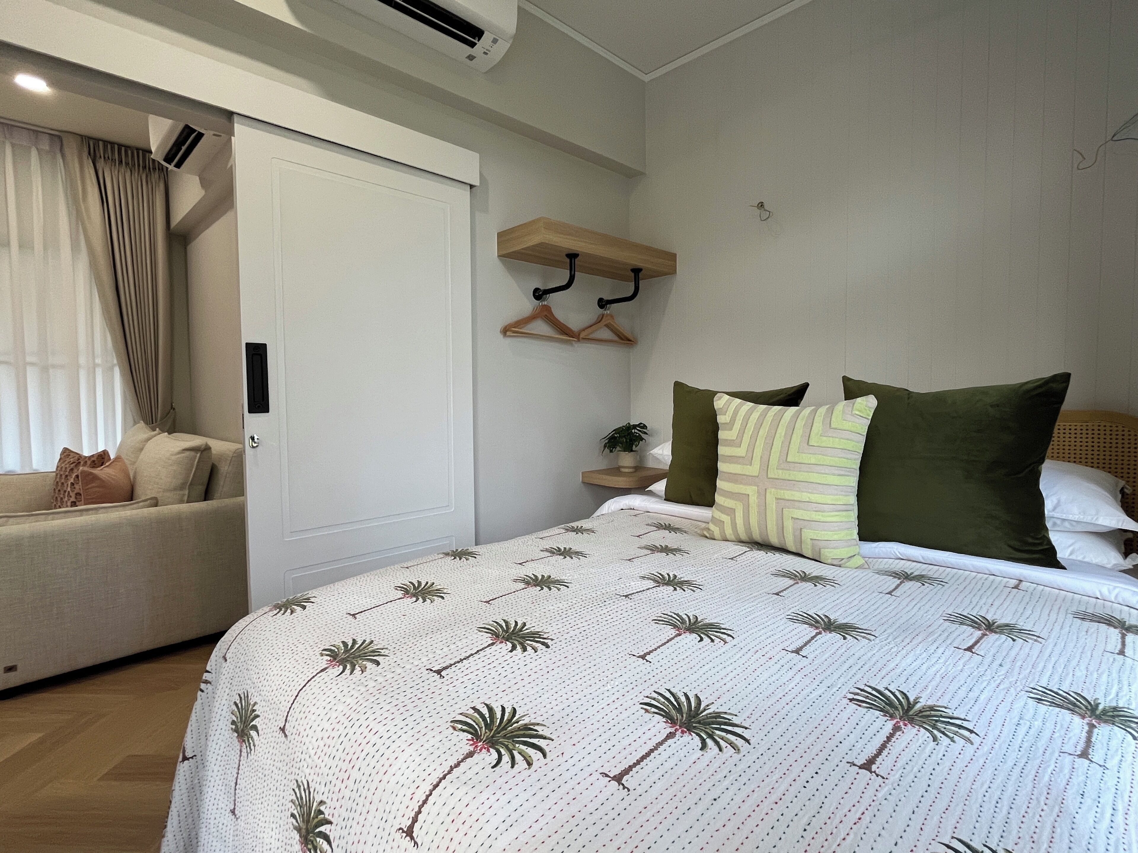 A bedroom with a bed, a sofa, a hanging plant, and a wooden shelf.