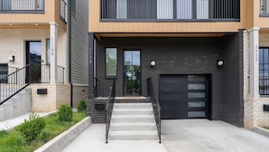 A modern two-story residential building with a concrete staircase, black railings, and a garage door. - Aloha Nashville🤙🏻~ Private Sauna & Hot Tub | Rooftop Oasis | City Views | Close to Broadway! (Nashville)