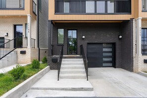 A modern two-story residential building with a concrete staircase, black railings, and a garage door. - Aloha Nashville🤙🏻~ Private Sauna & Hot Tub | Rooftop Oasis | City Views | Close to Broadway! (Nashville)