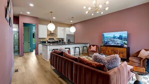 A modern living room with a sofa, a TV, and a kitchen area in the background. - Aloha Nashville🤙🏻~ Private Sauna & Hot Tub | Rooftop Oasis | City Views | Close to Broadway! (Nashville)