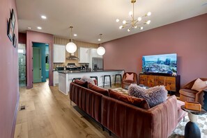 A modern living room with a sofa, a TV, and a kitchen area in the background. - Aloha Nashville🤙🏻~ Private Sauna & Hot Tub | Rooftop Oasis | City Views | Close to Broadway! (Nashville)