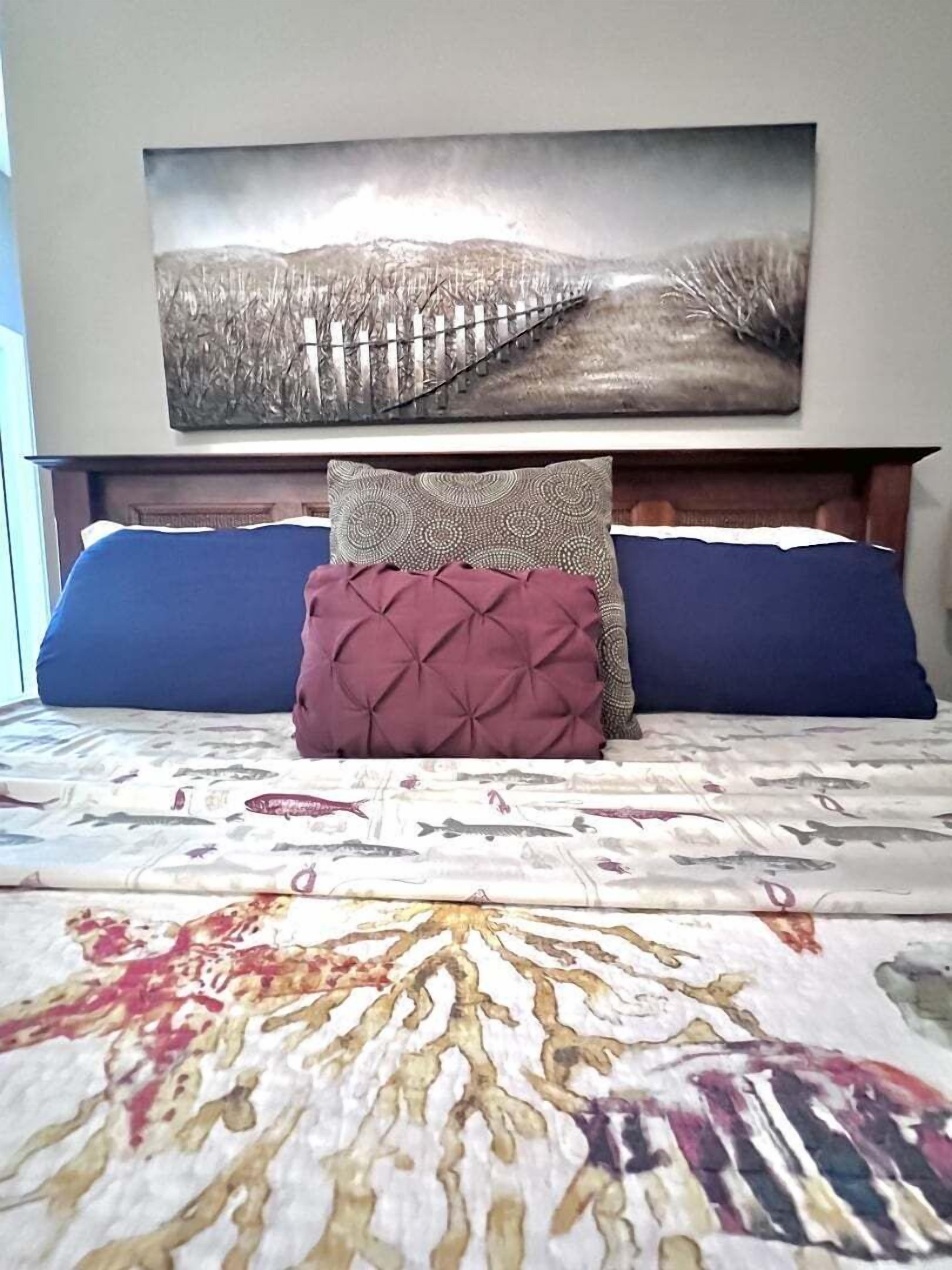 Een bed met een bedovertrek met patroon, twee kussens en een wanddecoratie erboven.