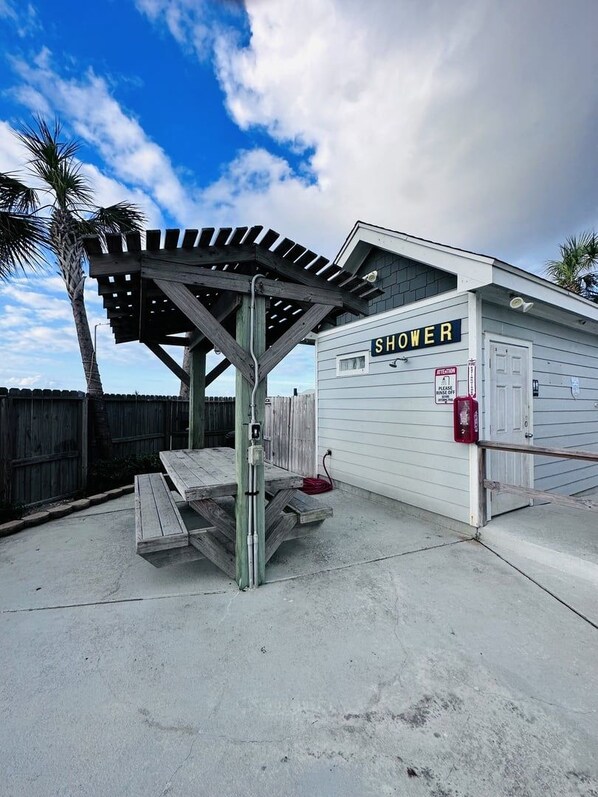 A portable shower structure with a wooden roof and a sign labeled 'SHOWER' on a concrete surface. - Salty Seashell, 3 Bedroom, Balcony Ocean View, Pool (Corpus Christi)