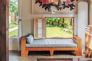 A room with a wooden bench, a window with a view of a garden, and a wall-mounted artwork. - Gangneung Orabdori Hanok Pension (Gangneung)