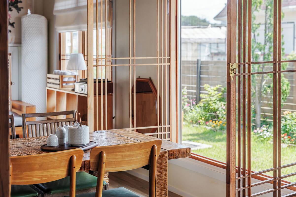 Un comedor con mesa de madera, sillas y vistas a un jardín a través de amplios ventanales.