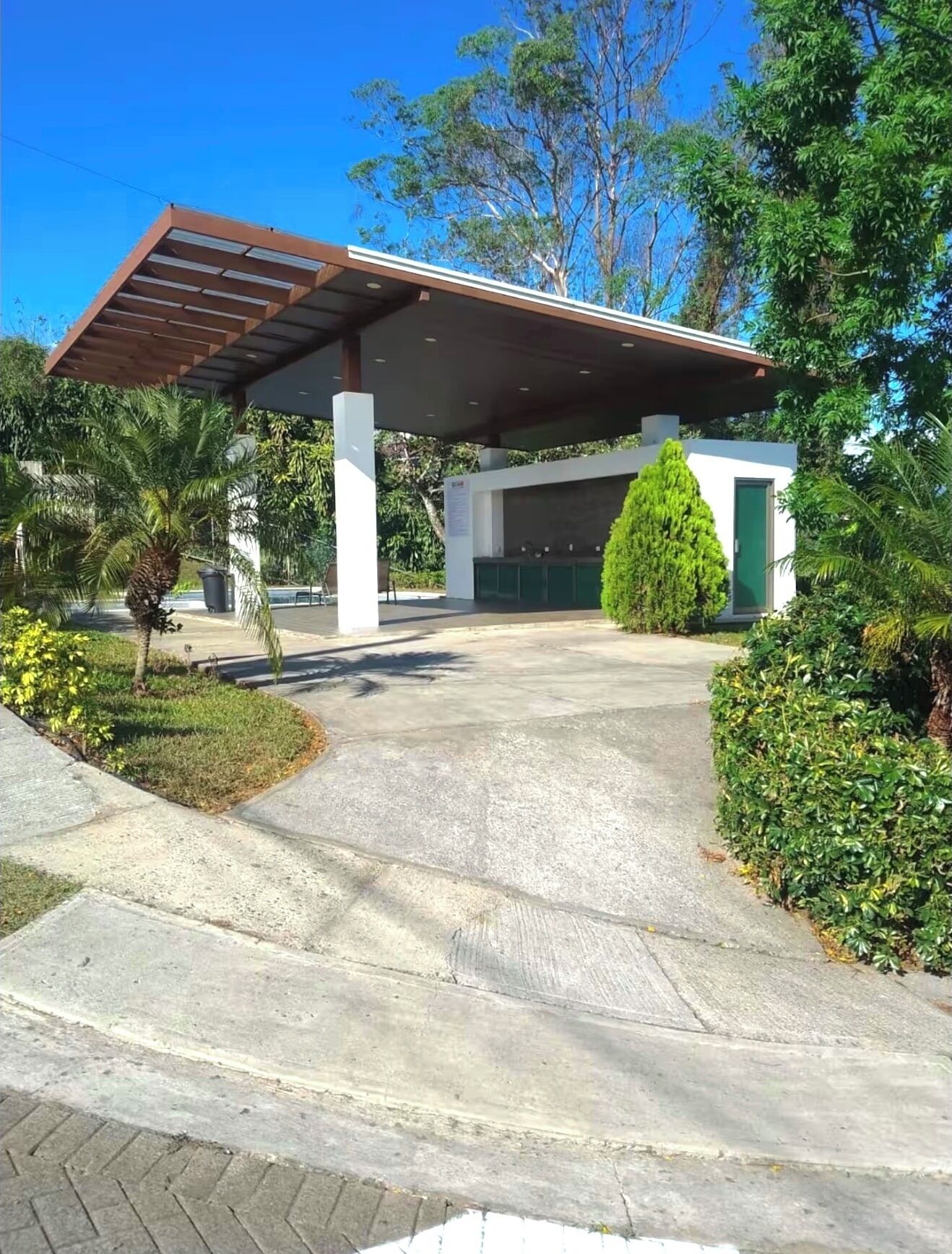 Un espace extérieur abrité, avec un chemin en béton menant à un bâtiment doté d’une porte verte.