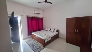 A bedroom with a bed, a wardrobe, a ceiling fan, an air conditioning unit, and a window with curtains.
