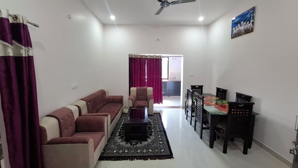 A living room with a sofa set, a coffee table, a dining table with chairs, a ceiling fan, and a view into the kitchen.