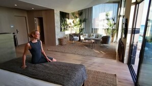 Ein modernes Hotelzimmer mit einem großen Bett, einer Sitzecke mit Sofa und Sesseln, einem kleinen Tisch und Blick auf den Ozean.