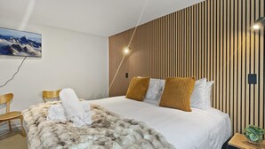 Una habitación de hotel moderna con una cama grande, un muro de listones de madera, un televisor montado y una mesita auxiliar con una planta.