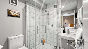 Un baño moderno con ducha de vidrio, inodoro, lavabo y espejo.
