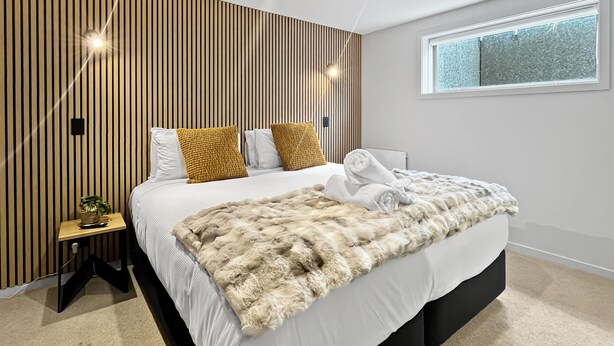 Un dormitorio moderno con una cama, un ventanal y una pared con listones de madera verticales.