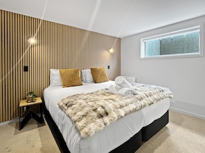 A modern bedroom with a bed, a window, and a wall with vertical wooden slats. - Smart Studio Stay | Great Value Location (Queenstown)