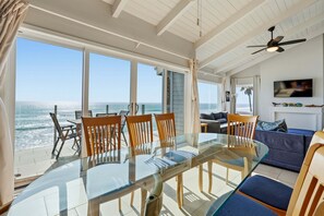 A room with a glass table and chairs, a sofa, a TV, and a ceiling fan. - Pacific Edge Retreat | Entire Estate, Ocean Views, Luxury Coastal Escape (Oceanside)