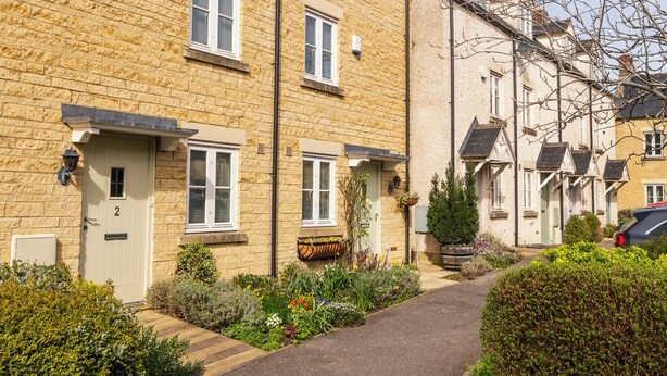 A row of terraced houses with a paved pathway, a small garden, and a clear sky. - Beautiful Two BD Home Near Cirencester (Stratton)