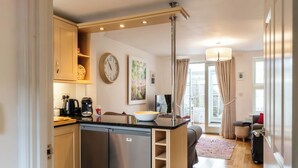 A compact kitchen with a refrigerator, coffee maker, and a bowl on the counter. - Beautiful Two BD Home Near Cirencester (Stratton)