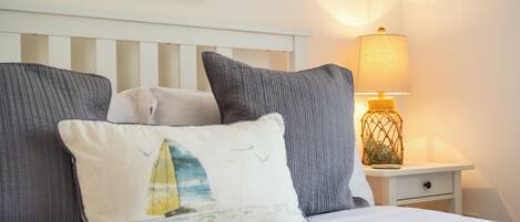 A bed with pillows, a nightstand with a lamp, and a wall with a floral painting.