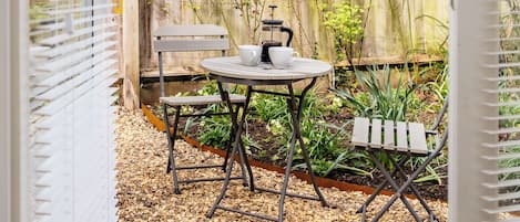 A patio with a table and chairs, a white fence, and a wooden deck.