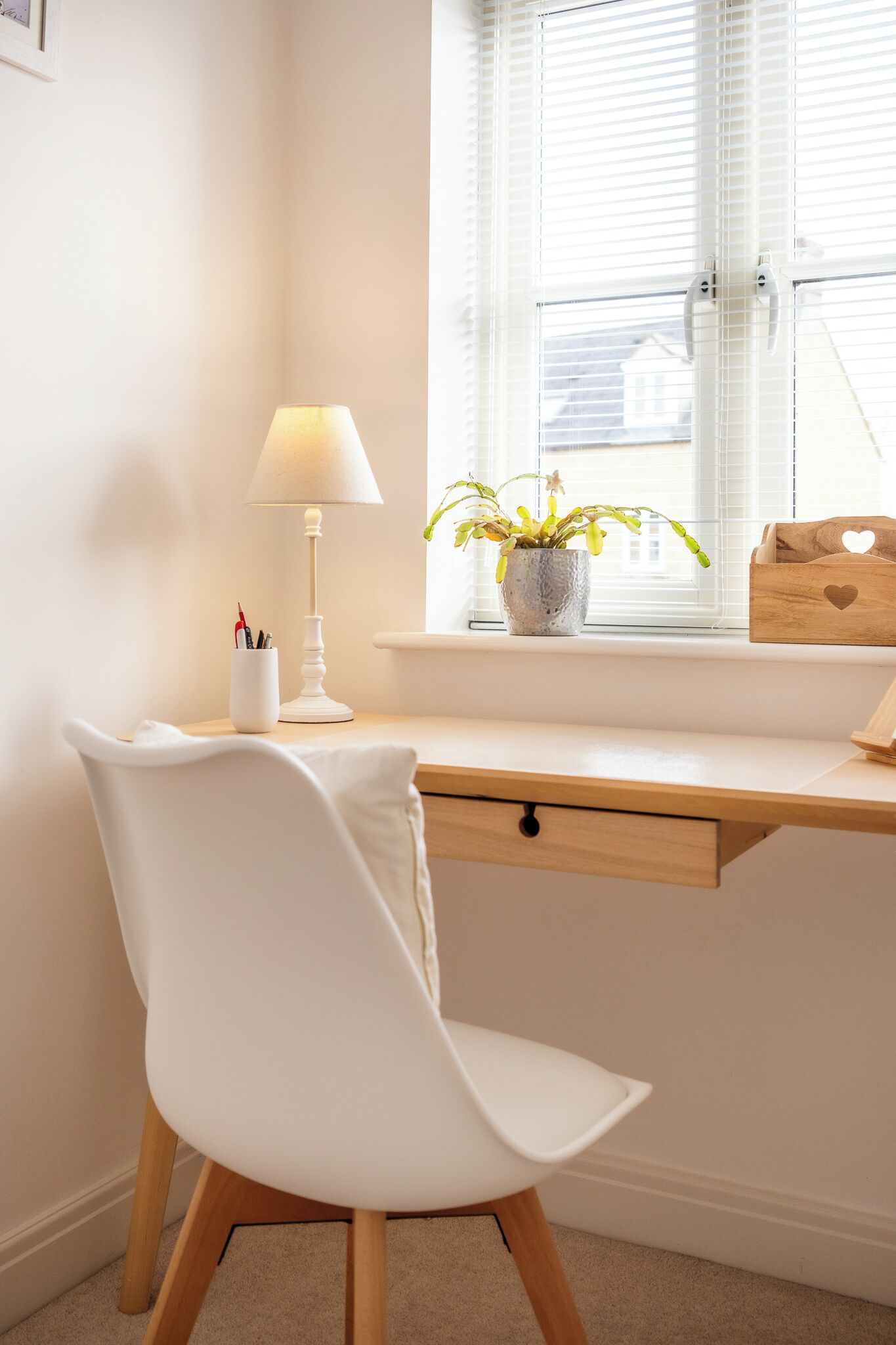 Ein weißer Schreibtisch mit Lampe, einer Topfpflanze und einer Holzkiste mit Herz-Ausschnitt.