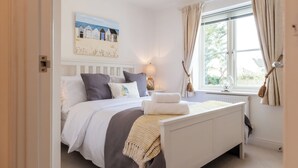 A bedroom with a bed, a painting, a window with curtains, and a radiator. - Beautiful Two BD Home Near Cirencester (Stratton)